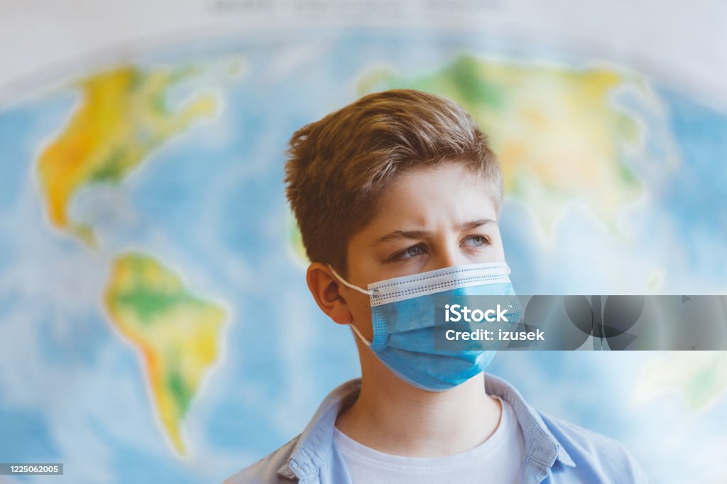 High school students at school, wearing N95 Face masks. A 13-year-old teenager wearing a N95 Face masks is standing in front of a world map 12-13 Years Stock Photo