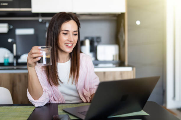istock Young woman using a laptop while drinking a cup of a coffee in her kitchen 1225063994