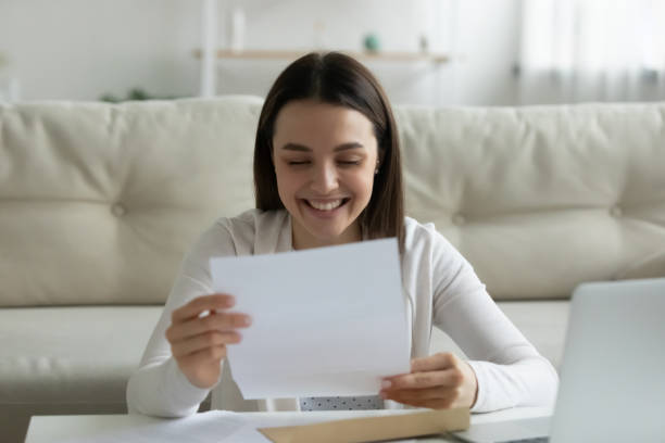 Happy young woman read good news in letter Happy millennial girl sit at home feel excited reading good news in postal paperwork letter, smiling young woman laugh enjoy pleasant positive response in post paper correspondence or notice college acceptance letter stock pictures, royalty-free photos & images