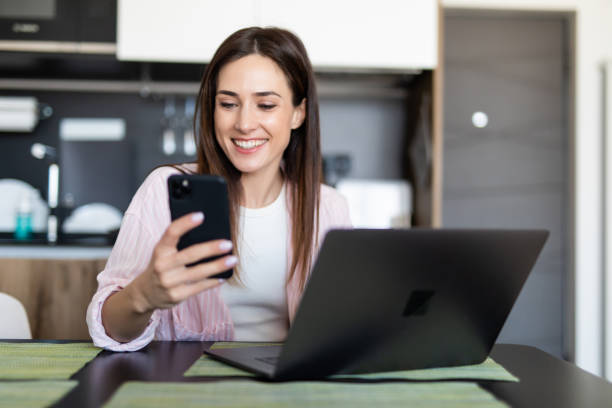 istock Young woman scroll phone while using laptop at table indoors 1225064564