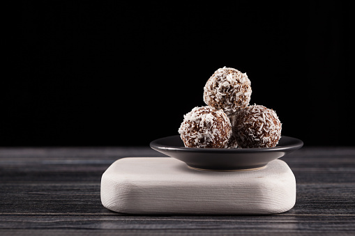 Energy balls with coconut, sweets proper nutrition homemade on dark background. Made from dates, apricots, almonds, pine nuts and prunes, with honey.  Dark wooden table, close-up, copy space.