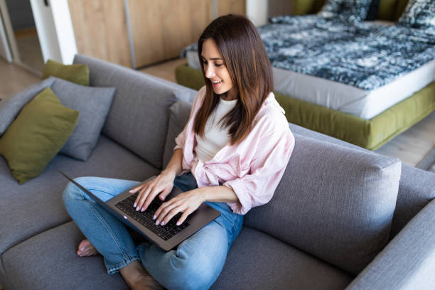 istock Happy pretty woman using laptop sitting on cosy sofa 1225067436
