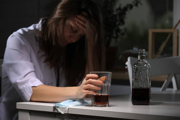 médecin féminin fatigué assis à la table et tenir le verre avec du whisky ou du cognac à la maison après le travail acharné, la femelle déprimée buvant de l’alcool fort souffrant de problèmes de coronavirus. - eastern european caucasian one person alcoholism photos et images de collection