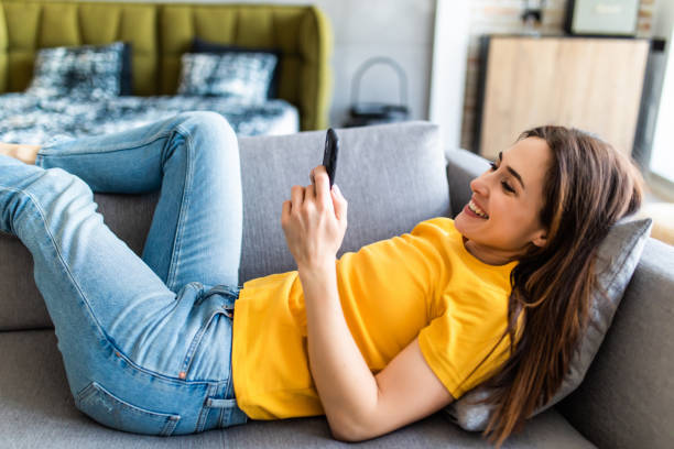 istock Attractive woman smiling as she reads an sms message on her mobile while relaxing on a sofa in her living room 1225070225