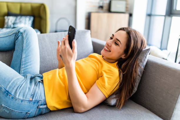 istock Attractive woman smiling as she reads an sms message on her mobile while relaxing on a sofa in her living room 1225072761