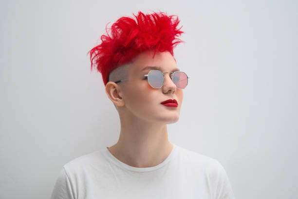 portrait of a cool fashionable modern young girl. a short haircut with shaved temple. dyed bright red hair. red lipstick. studio photo on white background. suspenders and checkered pants. - red hair hairstyle dyed hair women imagens e fotografias de stock