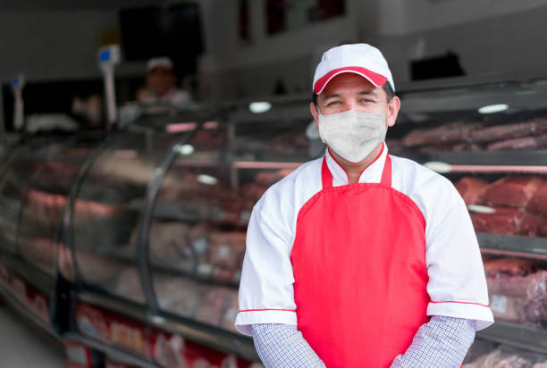 hombre trabajando en la carnicería con una máscara para evitar el coronavirus - delicatessen beef meat raw fotografías e imágenes de stock