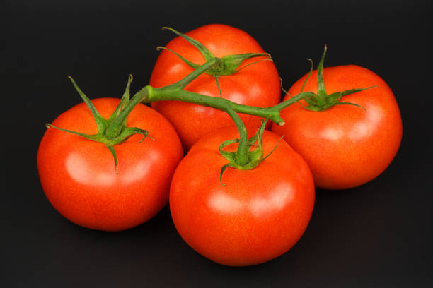 istock Four fresh juicy red bunch tomatoes on black background top view 1225076993