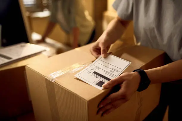 Photo of Close-up of deliverer attaching data label on cardboard box in the office.