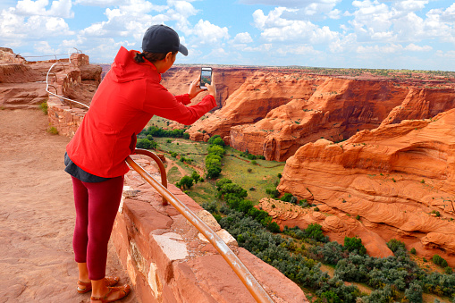 A young female visitor reaches over a hand rail and takes a picture with her smart phone at the Canyon de Chelly National Monument in eastern Arizona.