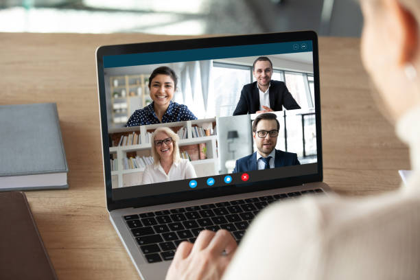 Computer screen view diverse businesspeople negotiating distantly using videocall View over female shoulder at computer webcam screen view of four different age and ethnicity business people negotiating distantly using video conference app, video call virtual communication concept webcam view man stock pictures, royalty-free photos & images