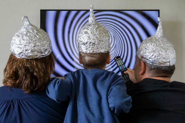 Family looks at the TV and has aluminium hats Family with Tin foil hat in front of TV tin foil hat stock pictures, royalty-free photos & images