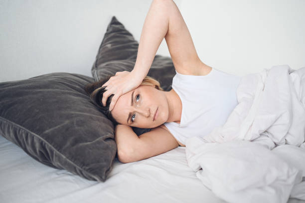 Depressed woman tormented by restless sleep, she is exhausted and suffering from insomnia, bad dreams or nightmares, psychological problems. Inconvenient uncomfortable bed or mattress. stock photo