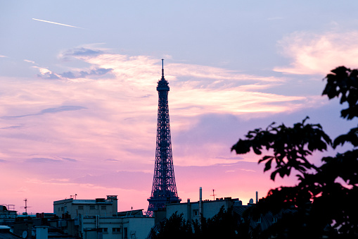 Top of Eiffel Tower against beautiful and colored sunset in background,  symbol of Paris and France.
