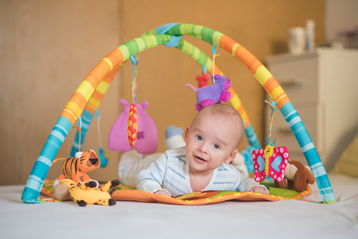 Cute baby boy, newborn, lying down on a bed and pmaxinh on play mat, baby gym, developing his skills. Curiosly looking at camera.