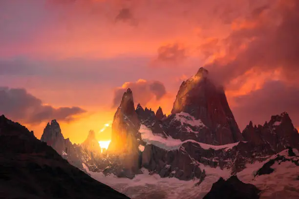 Rocky snowy mountain peaks with the sun rising behind and red clouds. Fritz Rroy in Argentina