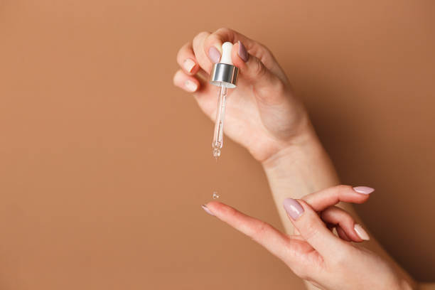 Hands of cropped white woman holding cosmetic serum pipette on the orange background stock photo