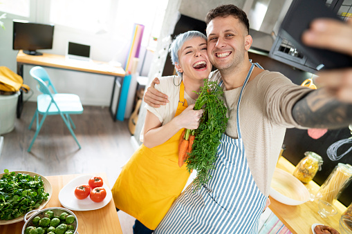 Love couple making a selfie while preparing healthy meal together at their kitchen.
