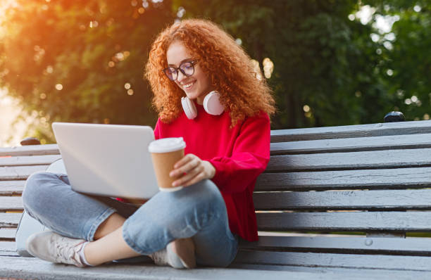 étudiant féminin de gingembre faisant des devoirs sur le banc - coffee to go flash photos et images de collection