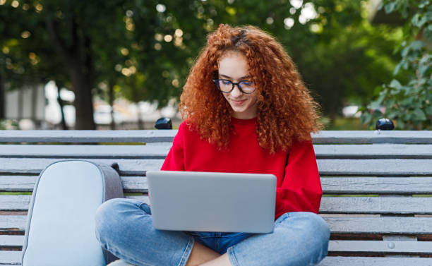 istock Smart female student using laptop in park 1225115755