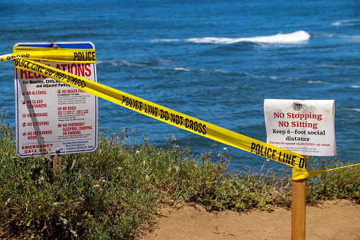 San Diego, CA USA May 14, 2020  Warning signs for social distancing and bright yellow police warning tape closing the paths along the cliffs and beach at Sunset Cliffs in San Diego