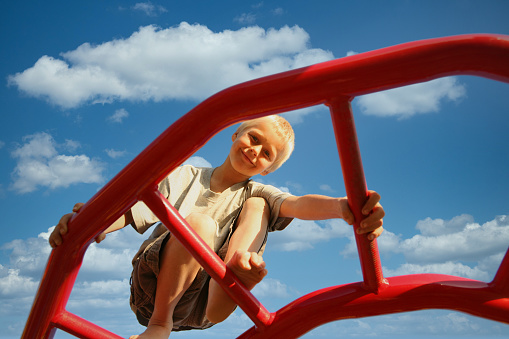 This is a photograph of a Boy on the Monkey Bars against a cloudscape