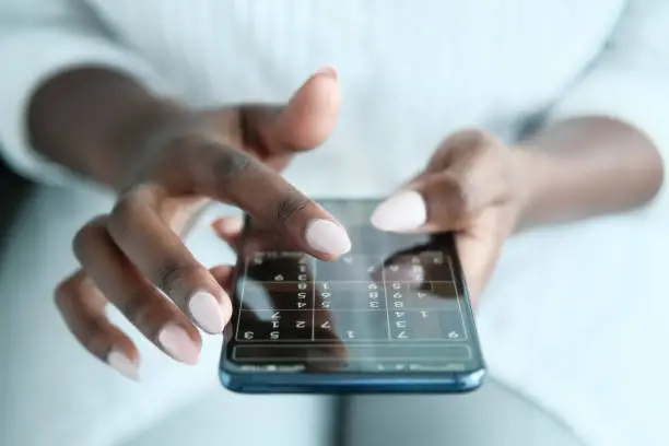 African American Woman Playing Sudoku Online For Brain Training, Using Mobile Phone. Cropped View, Closeup.