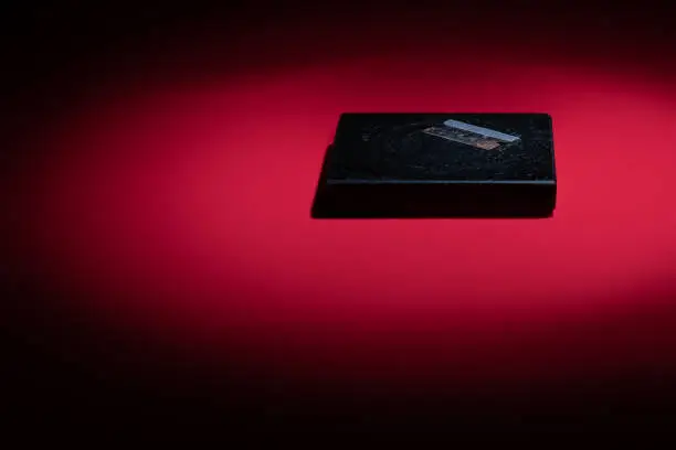 A clean light, almost ‘night time’ tint of blue light is focused on a dirty, rusty razor blade sitting on a used granite drink coaster, altogether spotlit on a red background. The image could possibly be used for drugs, cocaine use or other darker projects. The objects are placed so as to allow for copy space.
