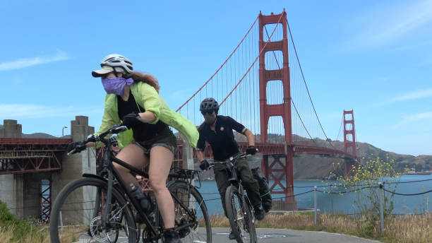 San Francisco, CA - May 15th, 2020: Bicyclists wearing face masks are riding the trail at Golden Gate Bridge during the covid virus emergency.