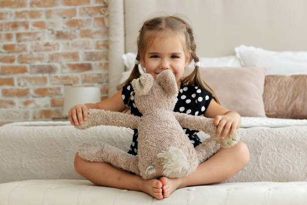 Cute little girl in black and white dress hugging her toy hare on the bed, happy childhood concept, indoor horizontal portrait