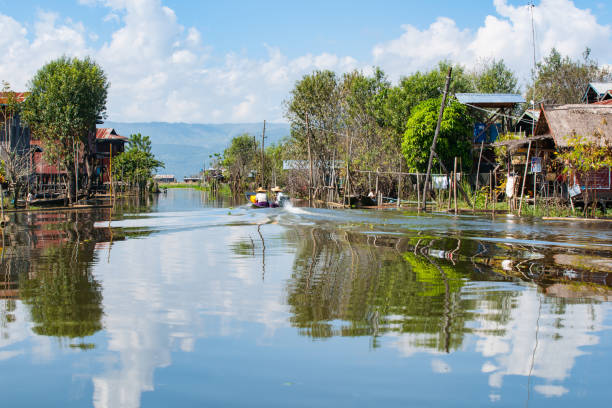 les habitants d’inle lake se sont entraînés dans un petit bateau jusqu’à la chaîne entre les maisons du village flottant. - motoring photos et images de collection