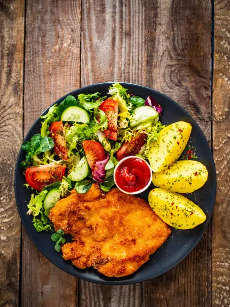 Fried pork chop, boiled potatoes and vegetable salad on wooden backgound