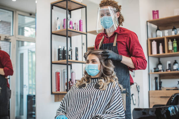 Young woman have hair cutting at hair stylist during pandemic isolation, they both wear protective equipment