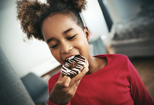 Closeup of a cute African American girl eating a chocolate glazed donut.