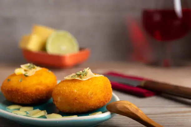 Homemade croquettes filled with cheese with lemon and a glass of red wine.