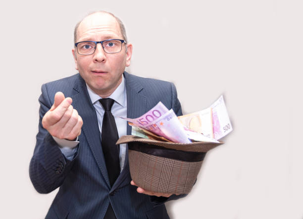 A man in a suit and glasses holds a hat in his hands and a lot of money and asks for help. Shows a hand gesture. A Caucasian man in a business suit and glasses asks for money, a businessman, an official, a corrupt official. European man on a gray background copy space civil servant stock pictures, royalty-free photos & images