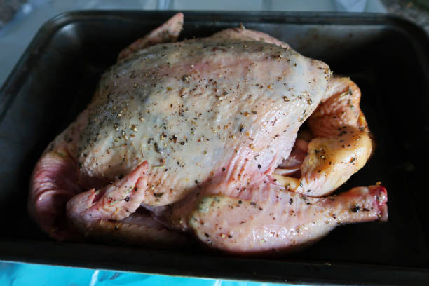 キッチンワークトップのオーブントレイにミックスハーブと挽いたコショウで覆われた鶏肉全体のクローズアップ画像、オーブン準備完了 - close up roasted meal pepper ストックフォトと画像