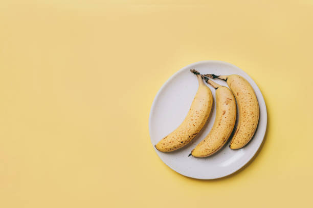 dojrzałe banany z brązowymi plamami na talerzu na żółtym tle - banana rotting ripe above zdjęcia i obrazy z banku zdjęć