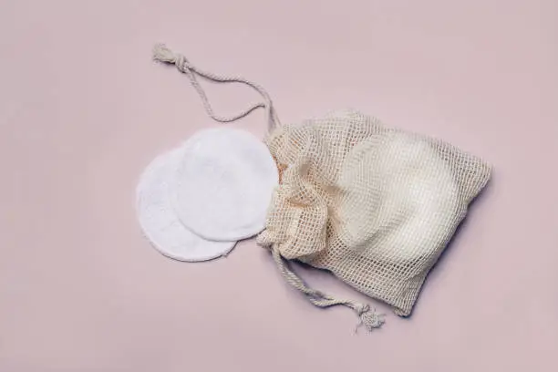 Photo of Reusable Bamboo Cotton Makeup Remover Pads in net bag on pink background. Zero-waste, sustainable lifestyle concept