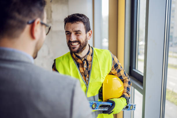 istock Smiling bearded contractor talking to businessman while standing in building in construction process next to window. 1225170848