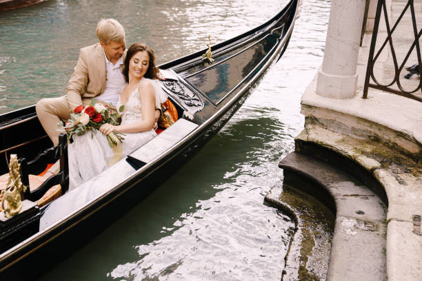 casamento na itália em veneza. os noivos andam em uma gôndola de madeira clássica ao longo de um estreito canal veneziano. close-up de abraços recém-casados. - shoe groom wood luxury - fotografias e filmes do acervo