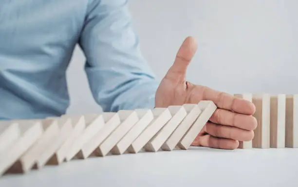 Close up of businessman stopping the domino effect on the wooden blocks with copy space