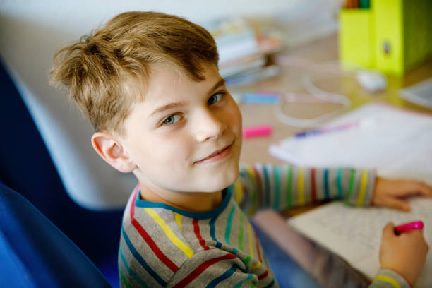 istock Hard-working happy school kid boy making homework during quarantine time from corona pandemic disease. Healthy child writing with pen, staying at home. Homeschooling concept 1225183546