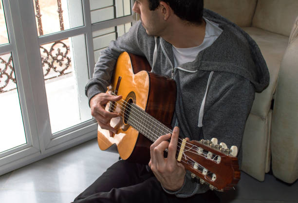 istock Melancholic young man watching the rain through a window while playing the guitar in a stormy day. 1225184911