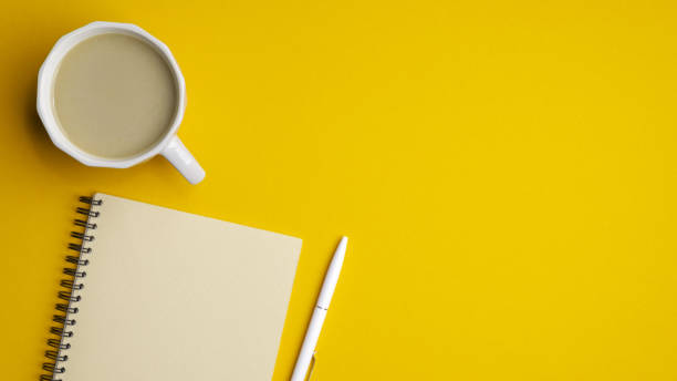 istock Modern office desk table with cup of coffee, notepad and pen on yellow background. Minimal style simple workspace. Top view with copy space, flat lay. Concept of business or education 1225185930