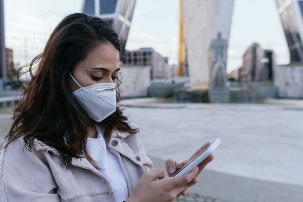 istock Young woman with phone messaging wearing mask 1225186198