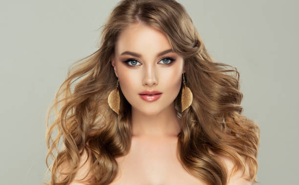 modella con acconciatura lunga, densa e liberamente posata e trucco pulito, orecchini dorati a forma di foglia vestiti nelle orecchie - big hair blond hair frizzy women foto e immagini stock