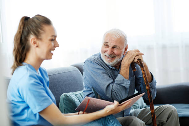 nurse doctor senior care brochure showing caregiver help assistence retirement home nursing elderly man Doctor or nurse caregiver showing a brochure to senior man at home or nursing home nursing home photos stock pictures, royalty-free photos & images