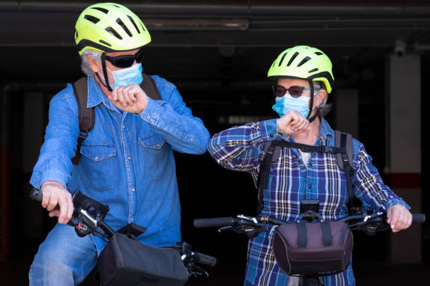 un couple sportif senior avec le vélo, un homme âgé et une femme, se saluent en touchant leurs coudes au lieu de serrer ou serrer la main. le covide-19 n’est pas encore terminé - cycling senior adult sports helmet men photos et images de collection