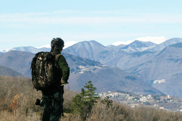 wanderer senior mann mit rucksack und kamera stehend auf dem berggipfel - aktiver reisender rentner mit grauen haaren - discovery reisezielkonzept, motivation - rückansicht mit kopierraum - behind photographer men mountain climbing stock-fotos und bilder